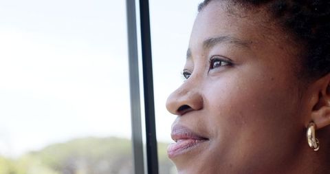 Contemplative african woman gazing through window with gold hoop earring