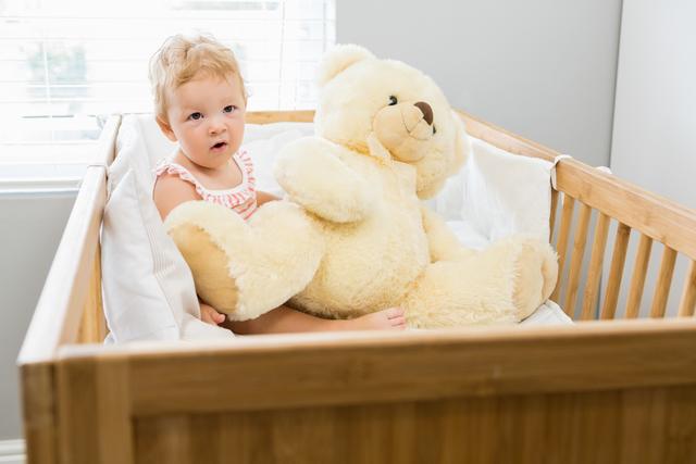 Baby girl playing with a teddy bear in a cradle at home