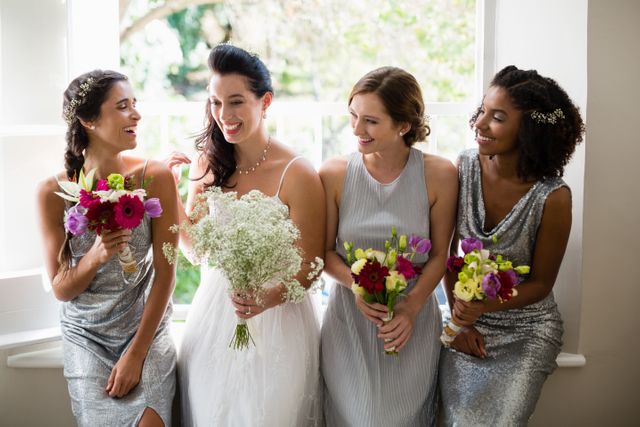Bride and bridesmaids standing together indoors, holding colorful bouquets and smiling. Ideal for wedding planning, bridal magazines, and celebration invitations.