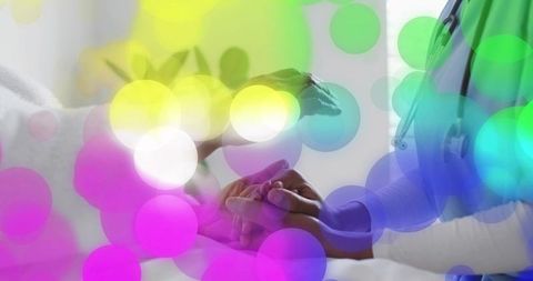 Nurse holding elderly patient hand providing comfort with colorful bokeh overlay