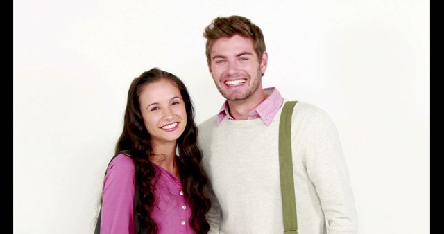 A happy young couple is smiling and posing together against a light background. They appear cheerful and casual, radiating positive energy. This can be used for lifestyle blogs, social media promotions, advertisements, or any content that aims to highlight happiness, relationships, and everyday casual moments.