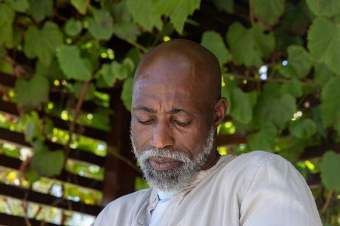 Contemplative african senior man sitting beneath vine-covered pergola sunlit garden patio
