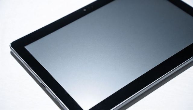Sleek black tablet resting on white tabletop displaying blank glass screen and camera
