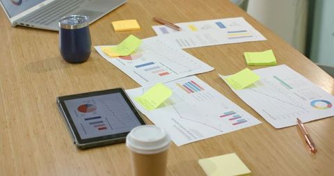Team analyzing business charts on wooden table with tablet, sticky notes and tumbler