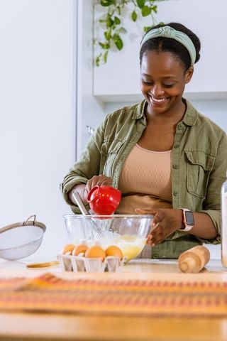 Smiling african american woman pouring from red cup and whisking batter for home baking