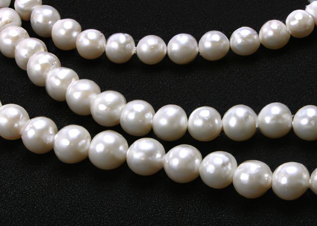 This image shows a close-up of multiple white pearl necklaces displayed against a black background. The shot highlights the smooth, lustrous surface of the pearls and conveys a sense of luxury and elegance. This image can be used in contexts related to fashion, jewelry advertisements, bridal accessories, upscale events, and online stores.