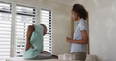 Senior man receiving back pain assessment from therapist in bright home therapy interior