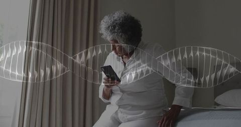 Senior woman using smartphone on bed while dna helix overlay representing genetic health tech