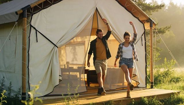 Couple stepping out of canvas glamping tent at sunrise celebrating outdoor adventure