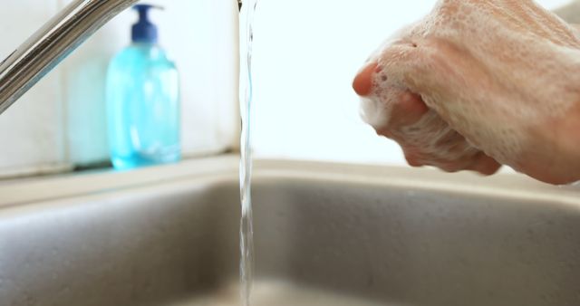 Person lathering hands with soap under running water in bathroom sink. Hand washing is essential for maintaining good hygiene and preventing the spread of illnesses and infections. This image can be used in articles, advertisements, and health campaigns promoting the importance of good personal hygiene and proper hand washing techniques. It is suitable for healthcare-related materials, public service announcements, and educational content focused on hygiene and cleanliness.