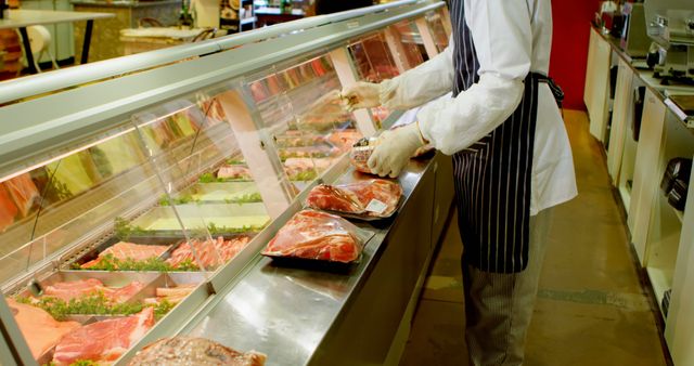 A butcher, middle-aged, is arranging various cuts of meat in a display case at a grocery store, with copy space. Their expertise ensures customers have access to fresh and well-presented selections of meat.