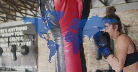 Female boxer training with heavy bag in industrial gym with world map data overlay