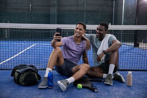 Multicultural friends taking selfie on indoor paddle court after match, smiling teammates