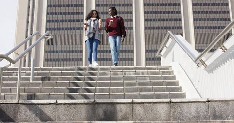 Young African American man and woman walking down city stairs holding takeaway coffee cups