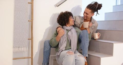 Cozy diverse couple sharing coffee on modern staircase, smiling and cuddling