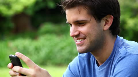 Smiling Man Enjoying Smartphone in Lush Green Park