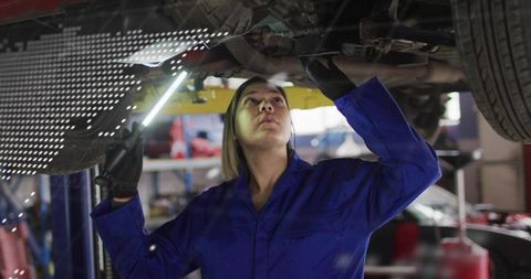 Female mechanic inspecting undercarriage on lift holding led work light in garage