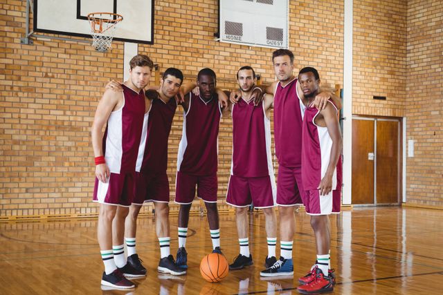 Group of confident basketball players standing together with arms around each other in an indoor court. They are wearing matching sports uniforms and displaying teamwork and unity. Ideal for use in sports-related content, team-building promotions, athletic advertisements, and articles on teamwork and sportsmanship.