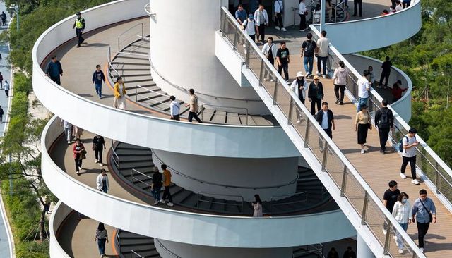 Pedestrians walking on elevated spiral ramp and wooden skywalk in urban park