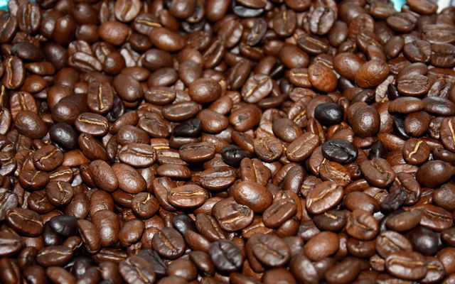 Close-up view of roasted coffee beans scattered densely, filling the entire frame. These shiny, brown beans have a rich texture and emit an aromatic feel, perfect for coffee-related promotions, café décor, beverage newsletters, and showcasing the artisanal aspect of coffee production.