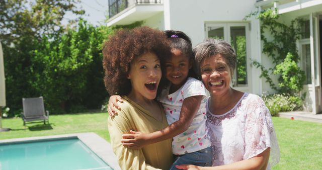 Portrait of happy biracial mother, daughter and grandmother embracing and smiling in sunny garden. Family, motherhood, lifestyle and togetherness.