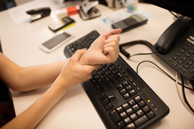 Businesswoman massaging her hand at office desk, indicating workplace stress or ergonomic issues. Useful for articles on office health, ergonomics, workplace wellness, and stress management. Ideal for illustrating concepts related to professional life, office work, and the importance of proper ergonomics.