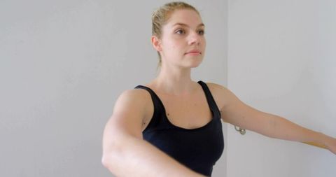 Young woman standing raising arms at barre wearing black tank for posture and balance