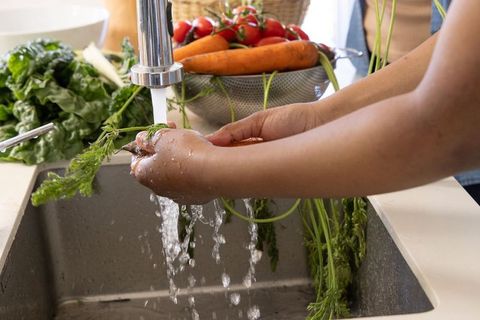 African american mother and teen daughter rinsing carrots at kitchen sink preparing healthy meal