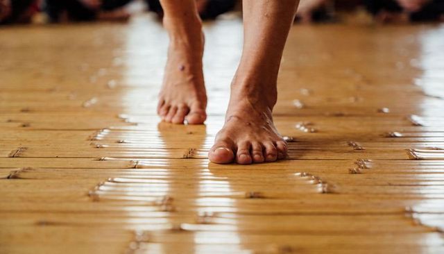 Bare feet stepping on glossy wooden plank floor close-up showing toes and arches