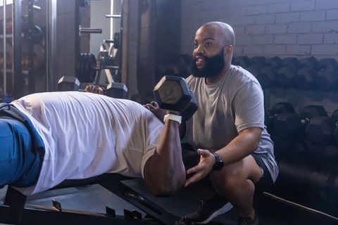 African trainer spotting client during dumbbell bench press coaching strength and focus