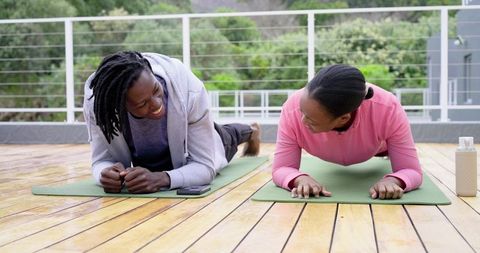 African American friends holding forearm planks on rooftop yoga mats, smiling in workout