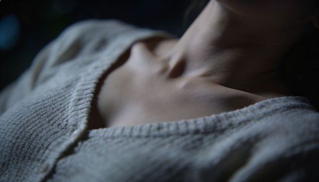 Intimate closeup of female collarbones and neck in soft knit v-neck sweater, moody interior