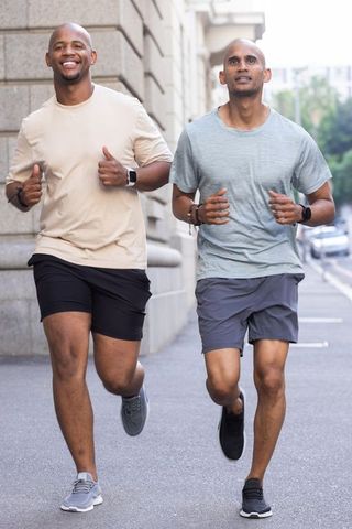 African american men jogging together on urban sidewalk wearing smartwatches and workout gear