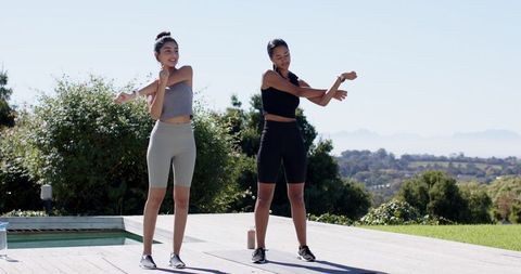Two Women Stretching in Outdoor Fitness Routine by Pool