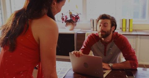 Casual office meeting with colleagues collaborating over laptop and design proofs