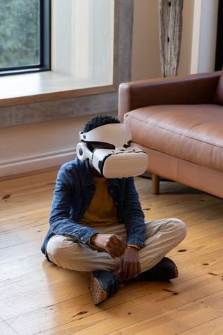 African American boy wearing VR headset sitting on wooden floor near leather sofa