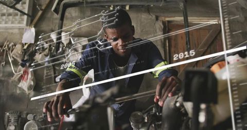 Hands-on mechanic leaning over engine repairing with long wrench in gritty industrial workshop