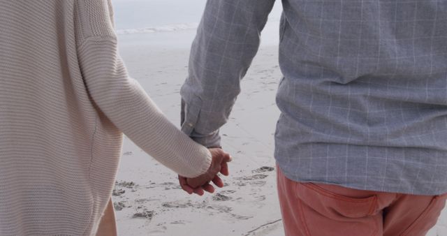 Midsection of senior african american couple holding hands and walking on beach. Senior lifestyle, summer and leisure, unaltered.