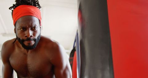 Determined Male Boxer Training with Punching Bag in Gym