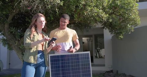 Young couple checking smartphone while testing residential solar panel in front yard