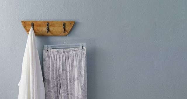 A minimalist wooden coat rack with metal hooks displays a towel and pants on a blue wall. - Download Free Stock Photos Pikwizard.com