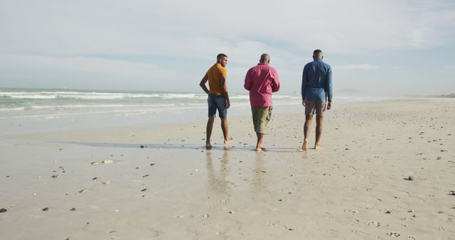 Three men are walking along a sandy beach on a sunny day. They appear to be enjoying the pleasant weather and each other's company, creating a relaxed and casual atmosphere. This image can be used for travel brochures, vacation promotions, lifestyle blogs, and advertisements focusing on leisure, friendship, and outdoor activities.