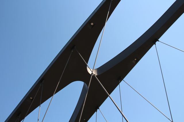 Capturing the sleek lines and structural elegance of a modern cable-stayed bridge against a clear blue sky. Perfect for usage in architectural presentations, engineering portfolios, urban development materials, and design projects showcasing modern infrastructure.