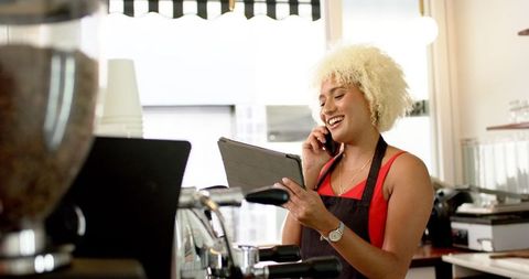 Young Barista Multitasking on Phone and Tablet in Coffee Shop