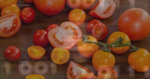 Displaying halved and whole red and golden tomatoes on rustic wooden table with vine and warmth