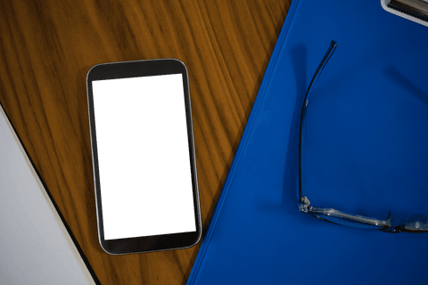High Angle of Mobile Phone and Blue Clipboard on Transparent Desk