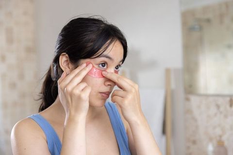 Asian woman applying pink under-eye hydrogel patches during morning skincare routine