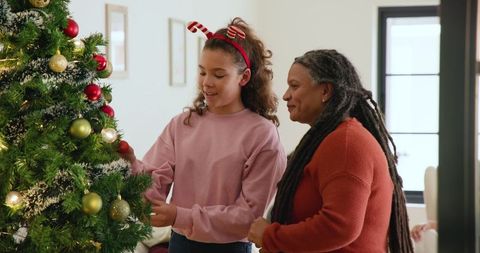 Grandmother and granddaughter decorating festive christmas tree at home