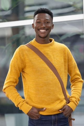 Smiling african american man wearing mustard sweater and crossbody bag in urban portrait