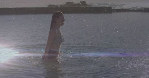 Woman leisurely wading through calm sunlit seawater at coastline